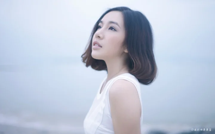 一名成年女性身穿白色無袖上衣，在柔和的藍色背景前側身仰望遠方。