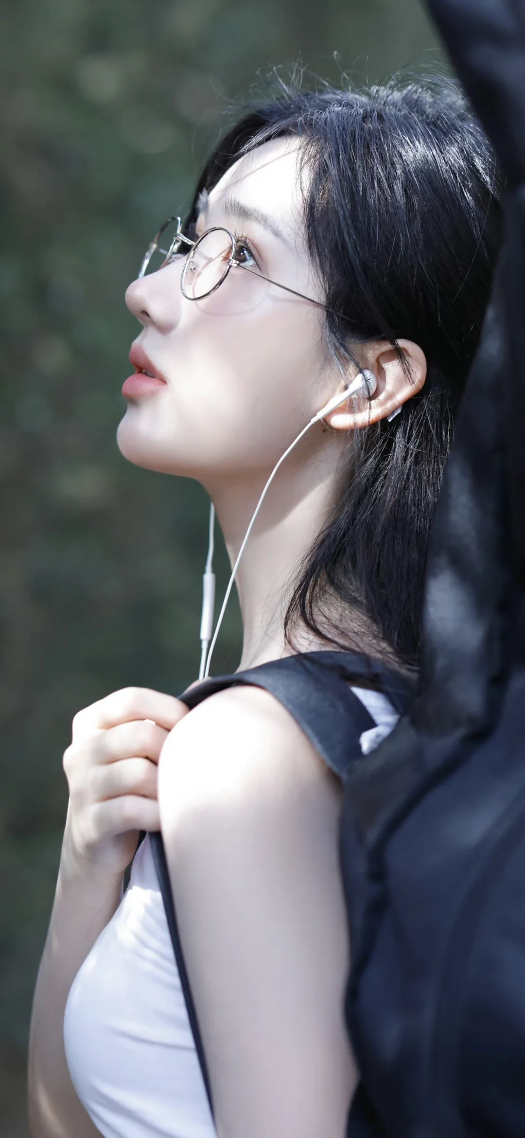 一名戴圆框眼镜并佩戴有线耳机的黑发女子侧脸望向上方。