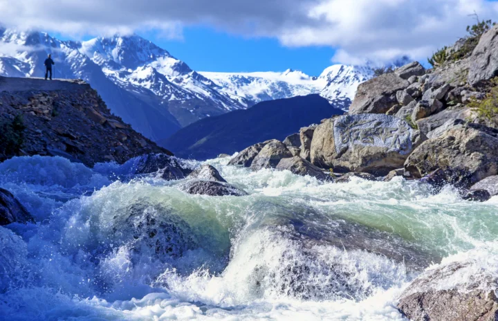 湍急的河水穿过岩石，远处是被云层环绕的雪山。