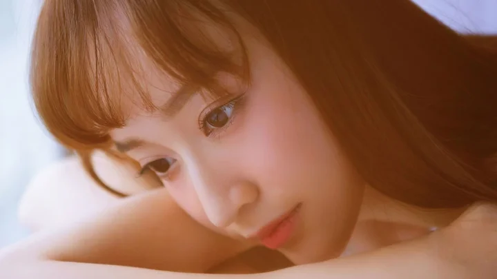 갈색 머리의 여성이 팔에 얼굴을 기대고 있는 부드러운 클로즈업 인물 사진입니다.