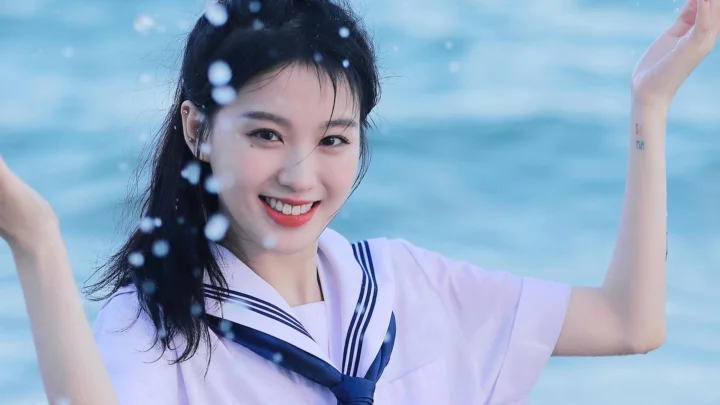 세일러 스타일 셔츠를 입은 여성이 푸른 물을 배경으로 미소 짓고 있다.