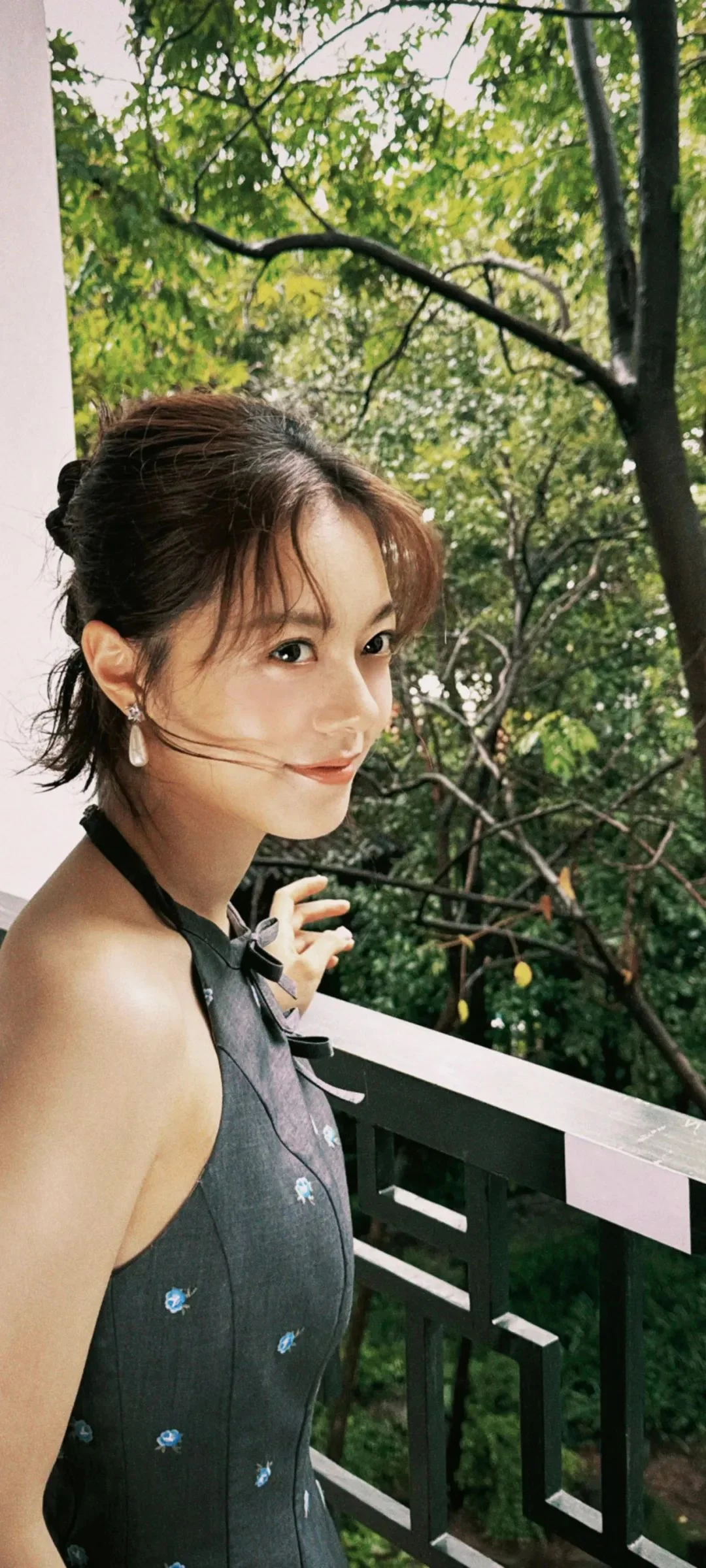 緑の木々に囲まれたテラスの手すりのそばに成人女性が立っています。