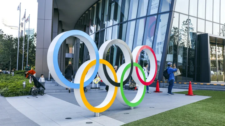 五彩奥运五环雕塑置于现代玻璃建筑前的户外广场上。