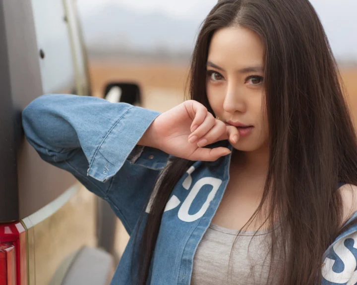 一名長髮女子穿著牛仔夾克，在車內面向鏡頭擺出肖像姿勢。