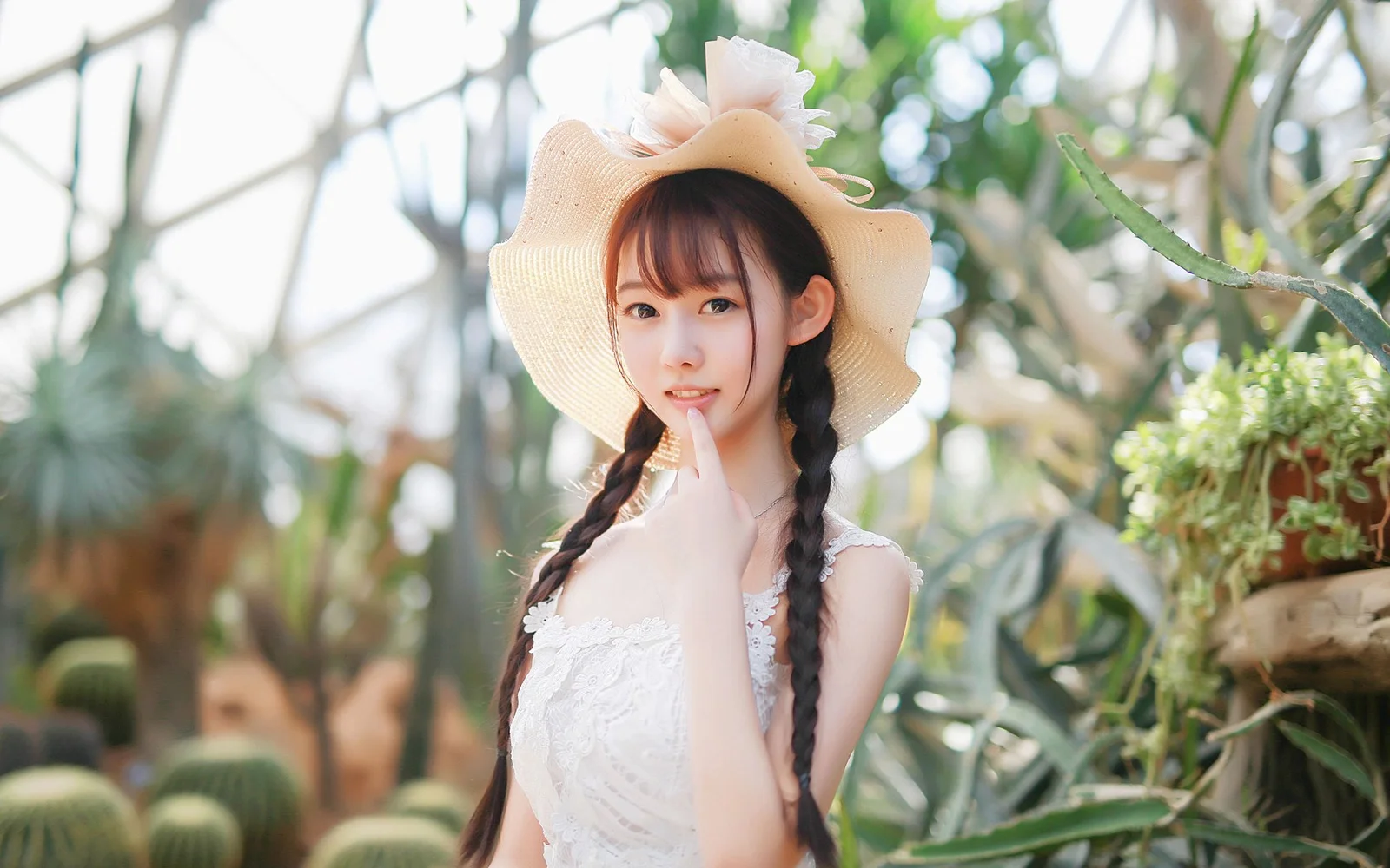 一名戴着宽檐帽、编着双辫的女子站在阳光明亮的温室植物间。