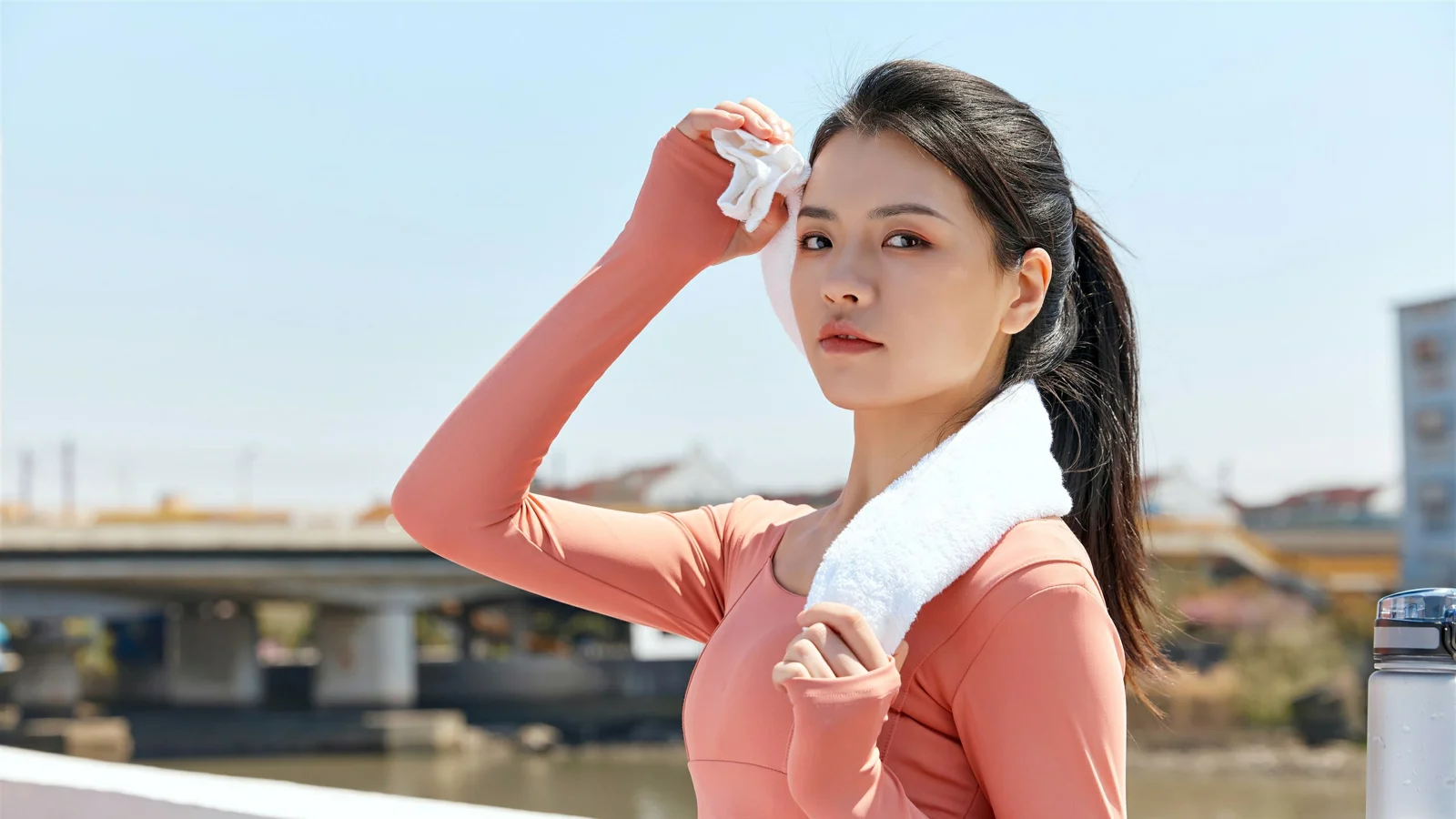 一名女性站在河畔户外，手持纸巾并搭着白色毛巾。