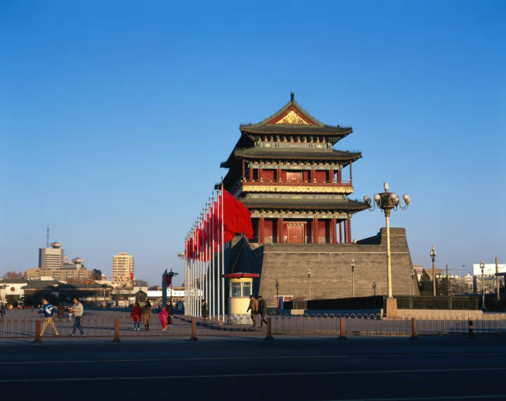 蓝天下，一座带有彩色屋檐和红色旗帜的传统建筑矗立在城市街道旁。
