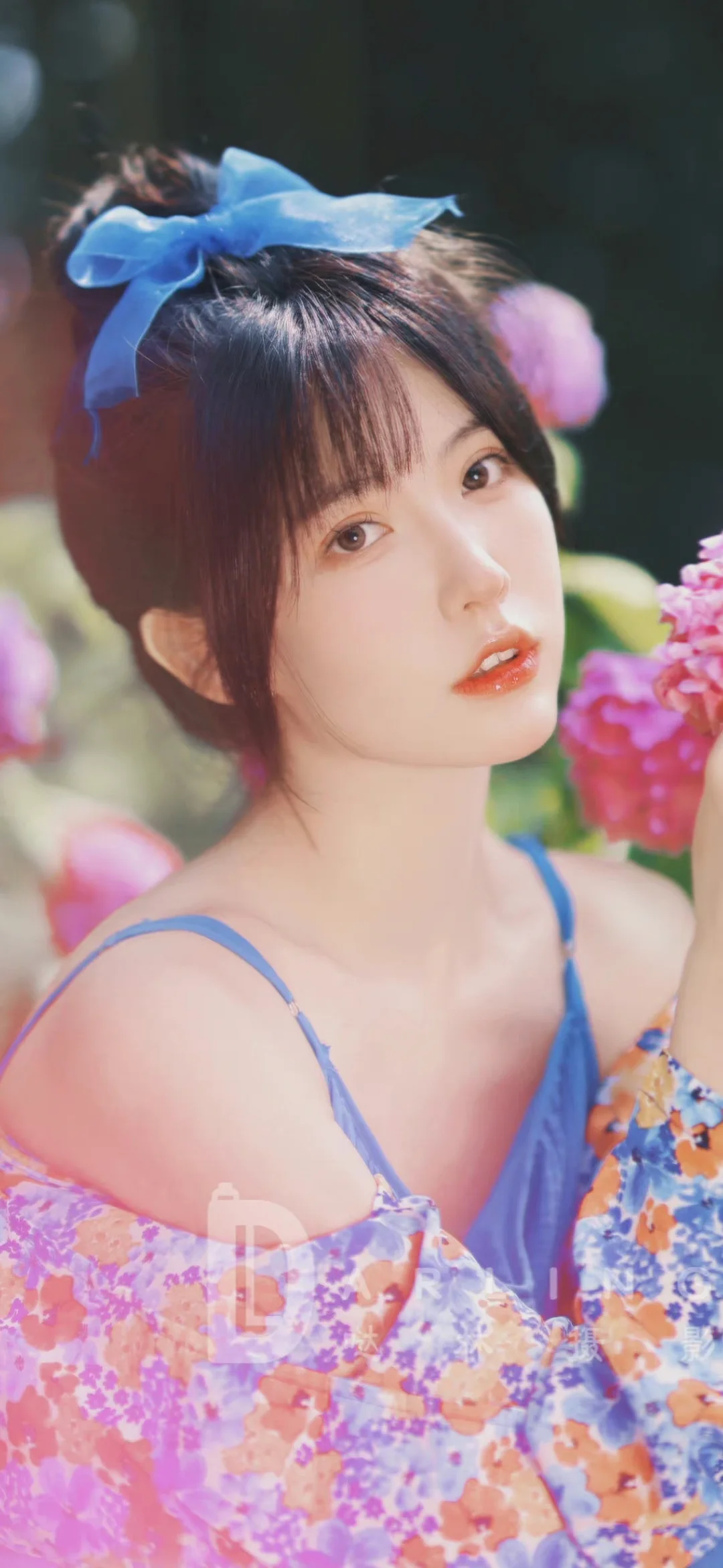 一名系着蓝色蝴蝶结、穿着蓝色吊带裙的女性站在花朵旁。