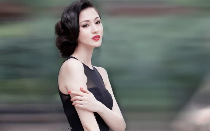 一位身穿黑色连衣裙的成年女性在模糊的绿色背景前交叉双臂。