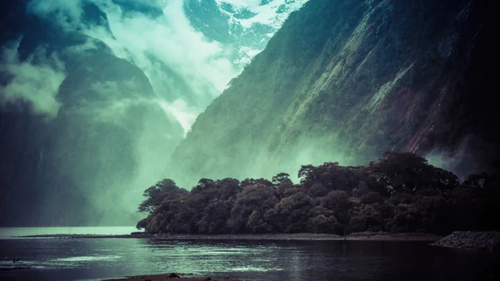 雾气笼罩的群山、森林与湖面构成一幅深色自然风景。