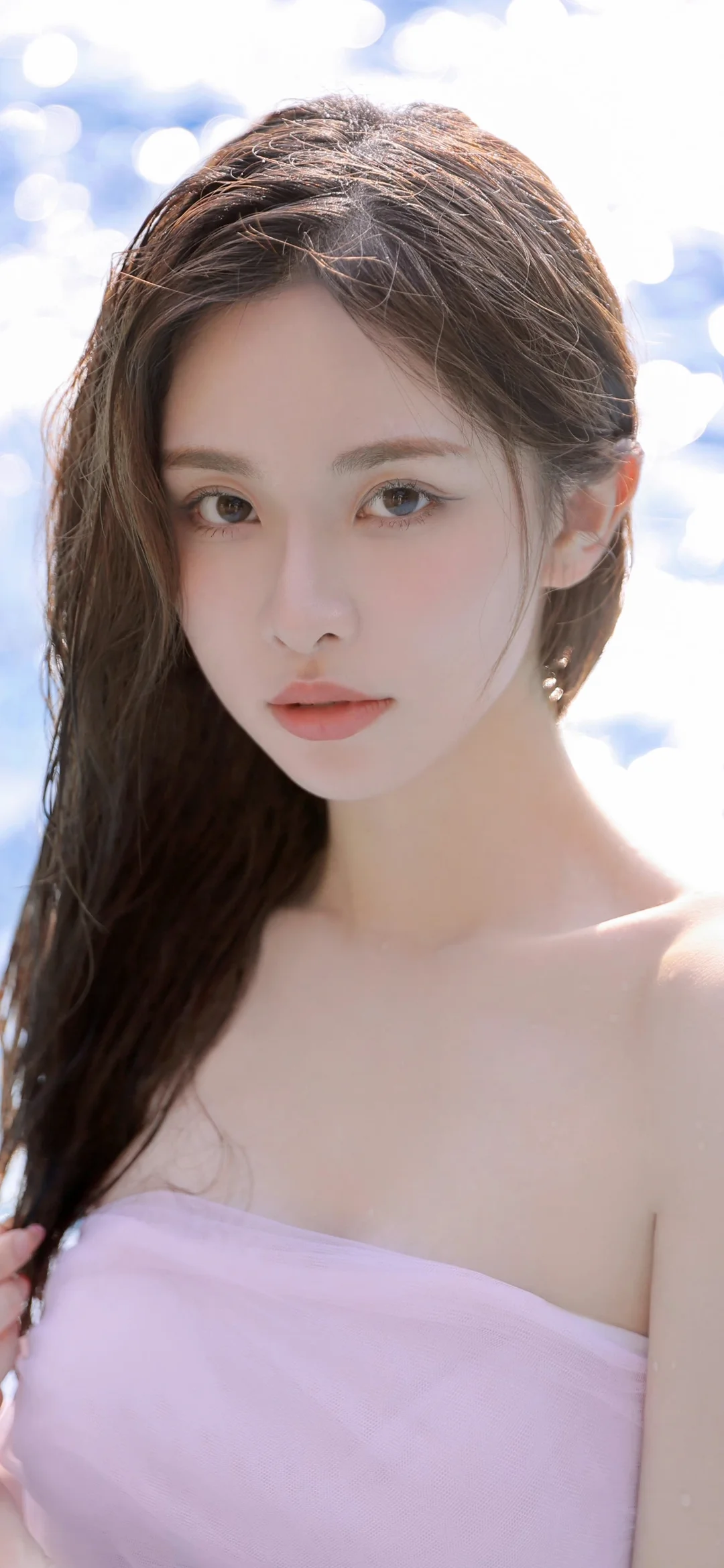 一位棕色长发女子穿着浅粉色露肩上衣，在明亮虚化背景前面对镜头。