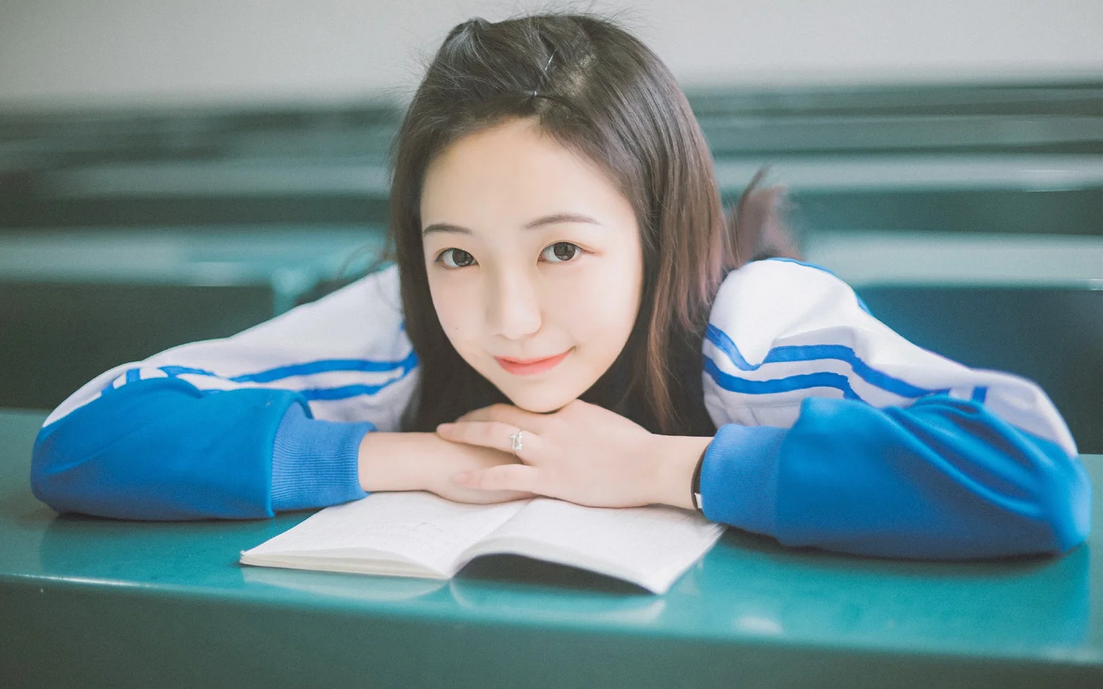 青いジャケットを着た女性が、開いた本のそばに腕を置いている。