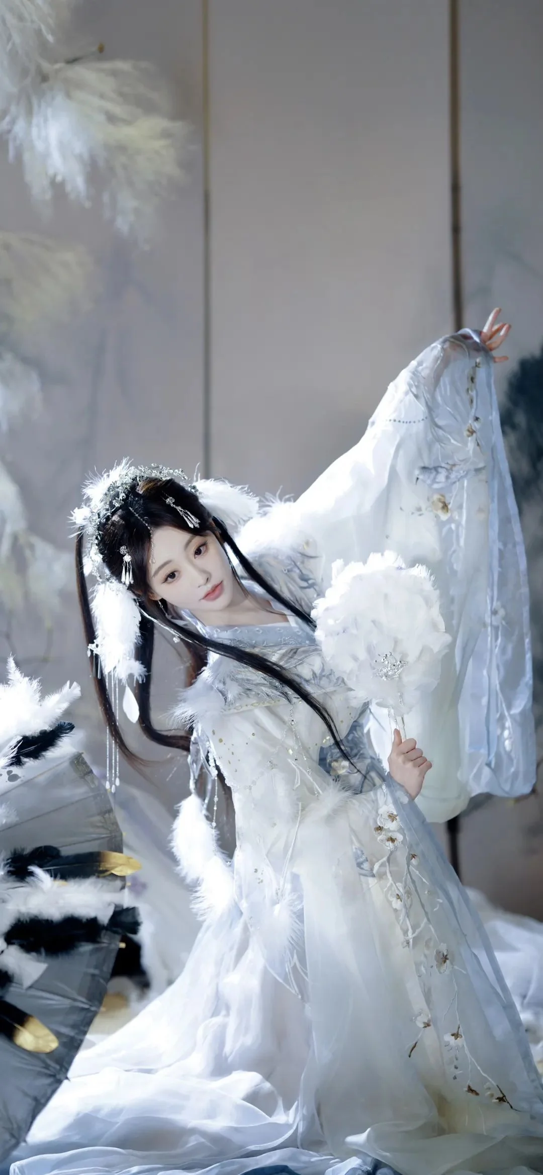 一位身穿白色传统风格服饰并佩戴羽毛装饰的女性站在室内。
