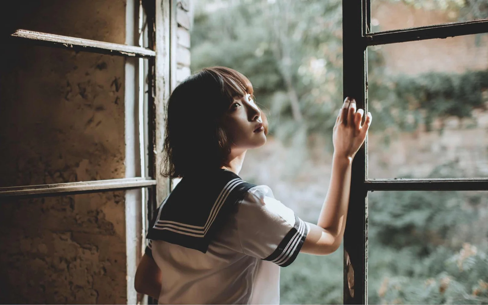 一名女性站在窗邊，回頭望向窗外的綠意。
