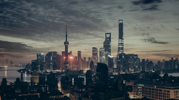 暮色中的现代城市天际线灯火初亮，临水高楼映衬着云层天空。