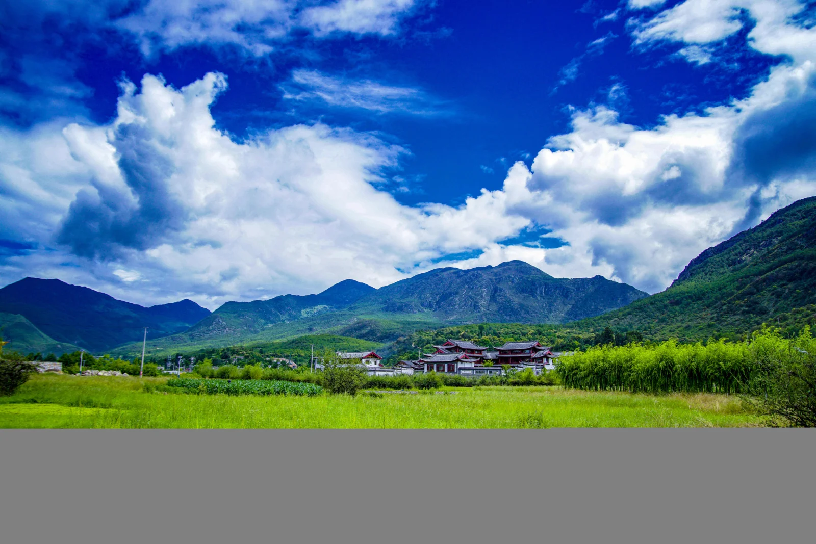 群山、白雲、綠色田野和遠處的傳統建築構成寧靜的山谷景色。