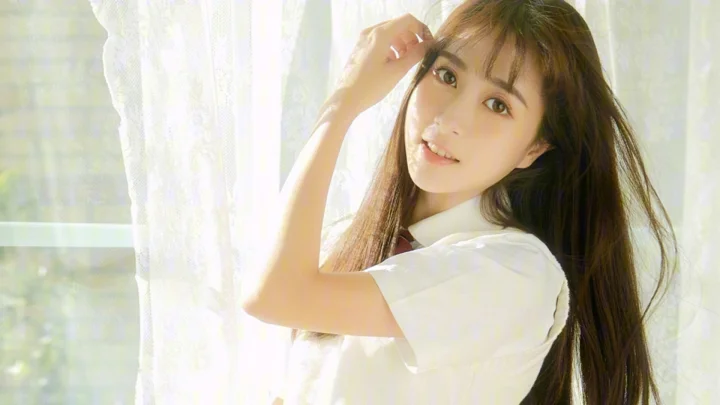 長い髪の女性が白いシャツを着て明るい窓辺に立っています。