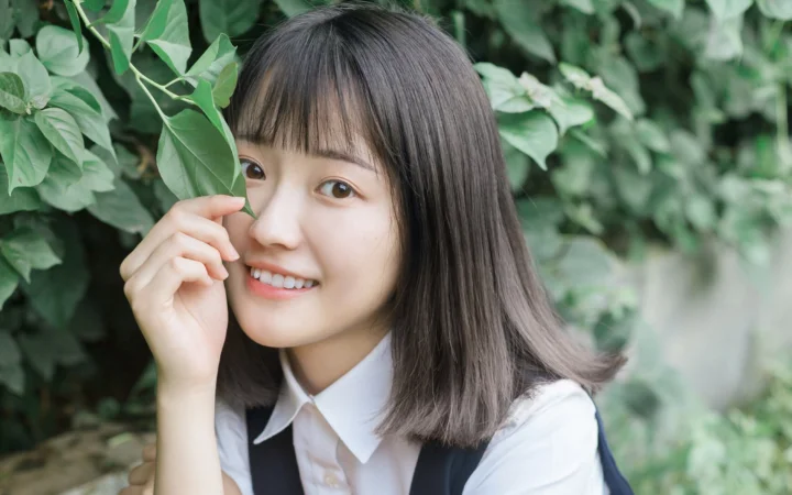 긴 머리의 여성이 초록 잎을 들고 푸른 식물을 배경으로 미소 짓고 있다.