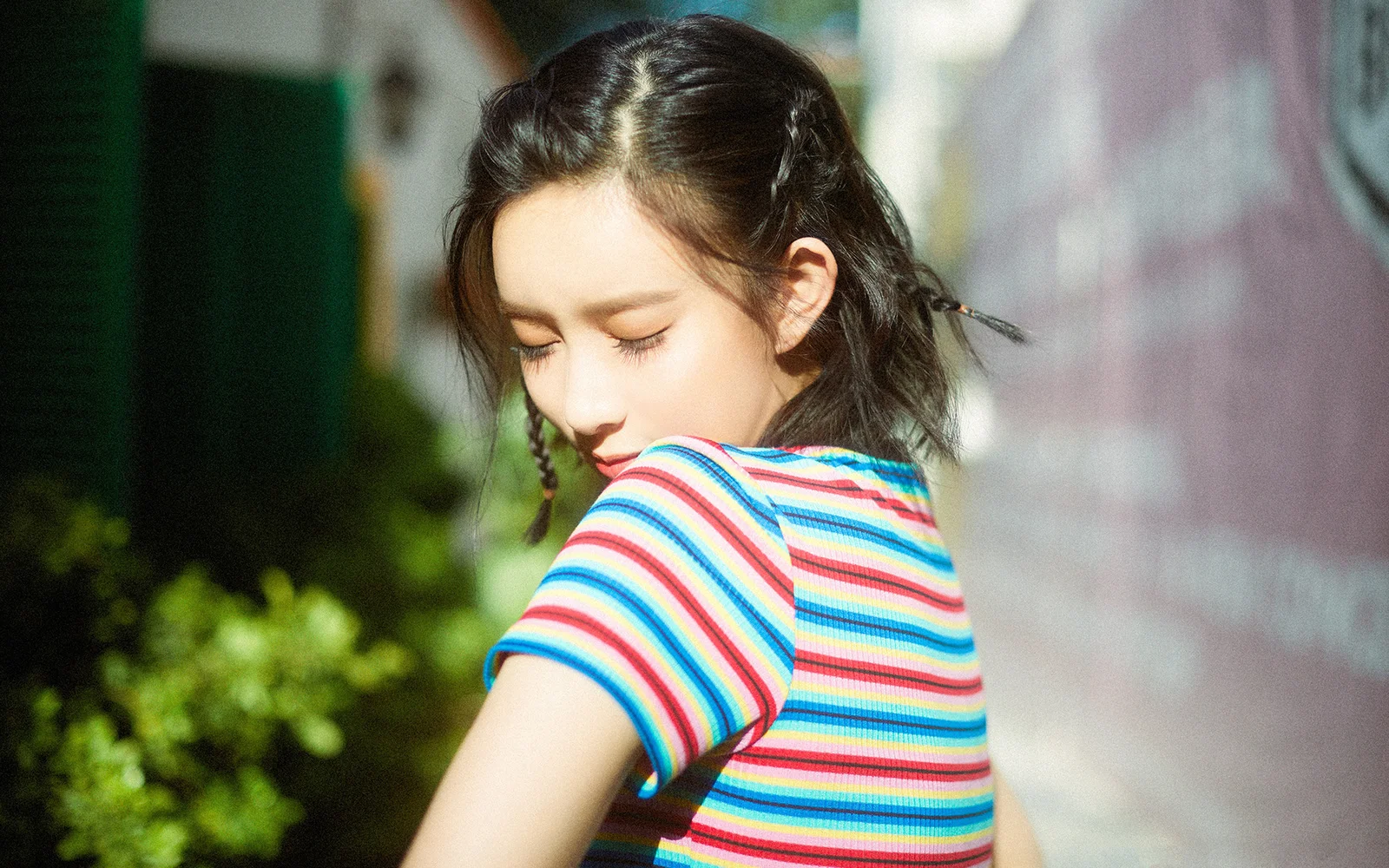 알록달록한 줄무늬 셔츠를 입은 여성이 야외 햇살 속에서 뒤돌아보고 있다.