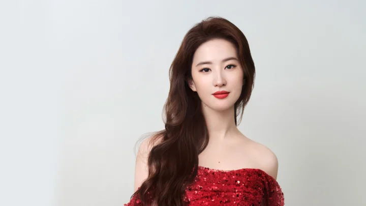 一名长发女性身穿红色亮片礼服，在浅灰色背景前面对镜头。