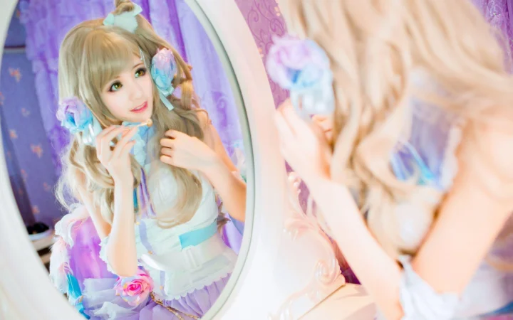 夢幻的な衣装を着た成人女性が鏡の前で髪を整え、鏡越しの姿が画面を占めています。