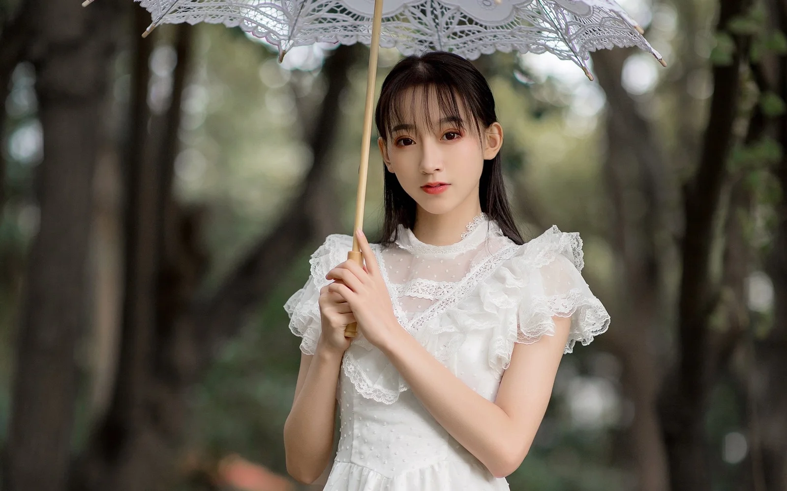 흰색 레이스 상의를 입은 여성이 숲속에서 레이스 우산을 들고 있다.
