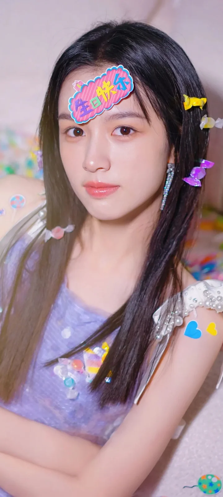 一名长发女性佩戴彩色发饰和贴纸，身穿浅紫色上衣面对镜头。