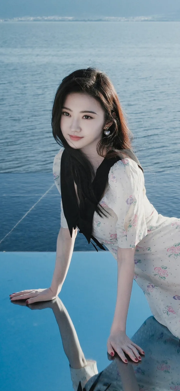 一名女子在海边蓝色平台上摆 pose，身后是平静的海面。