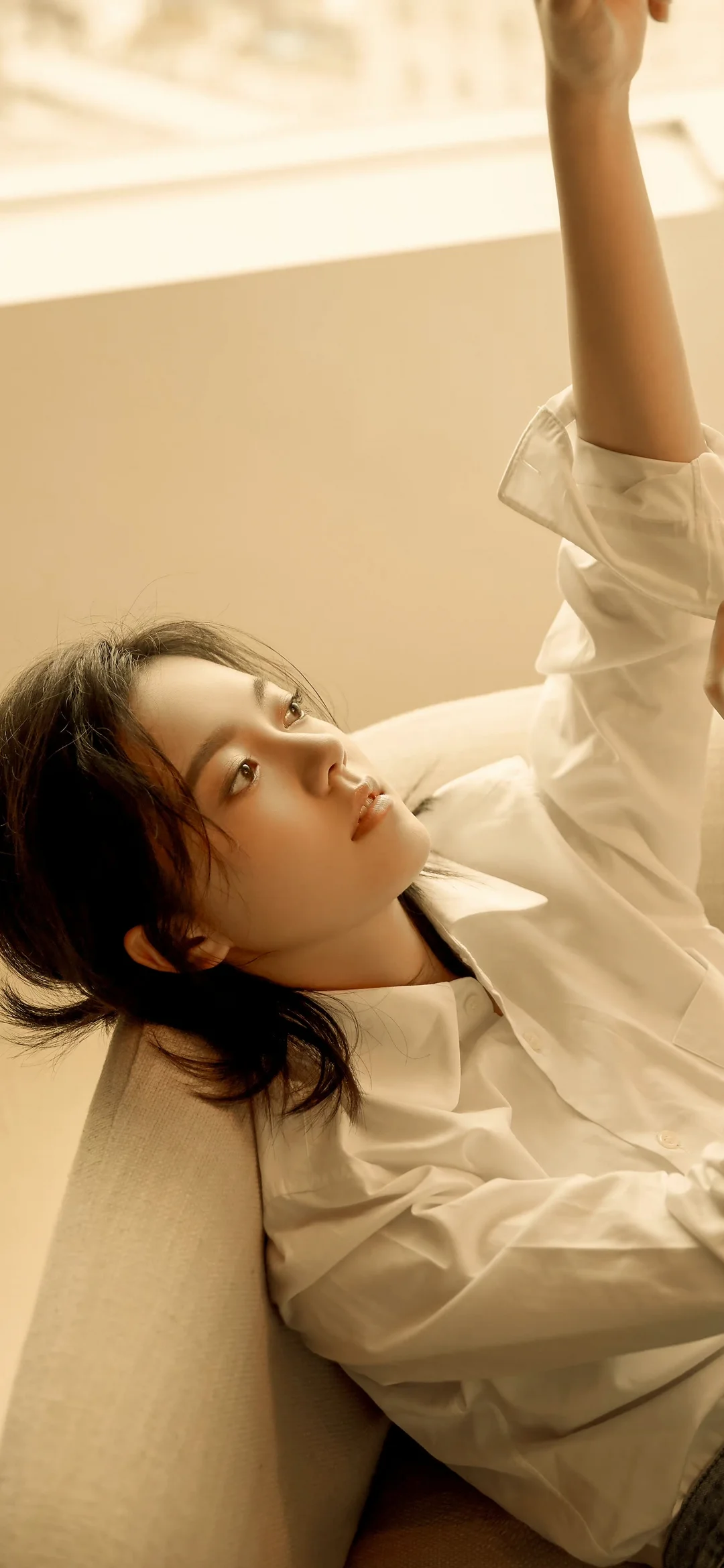 一名成年女性穿着白衬衫倚靠在沙发上，室内暖光勾勒出她的侧脸。