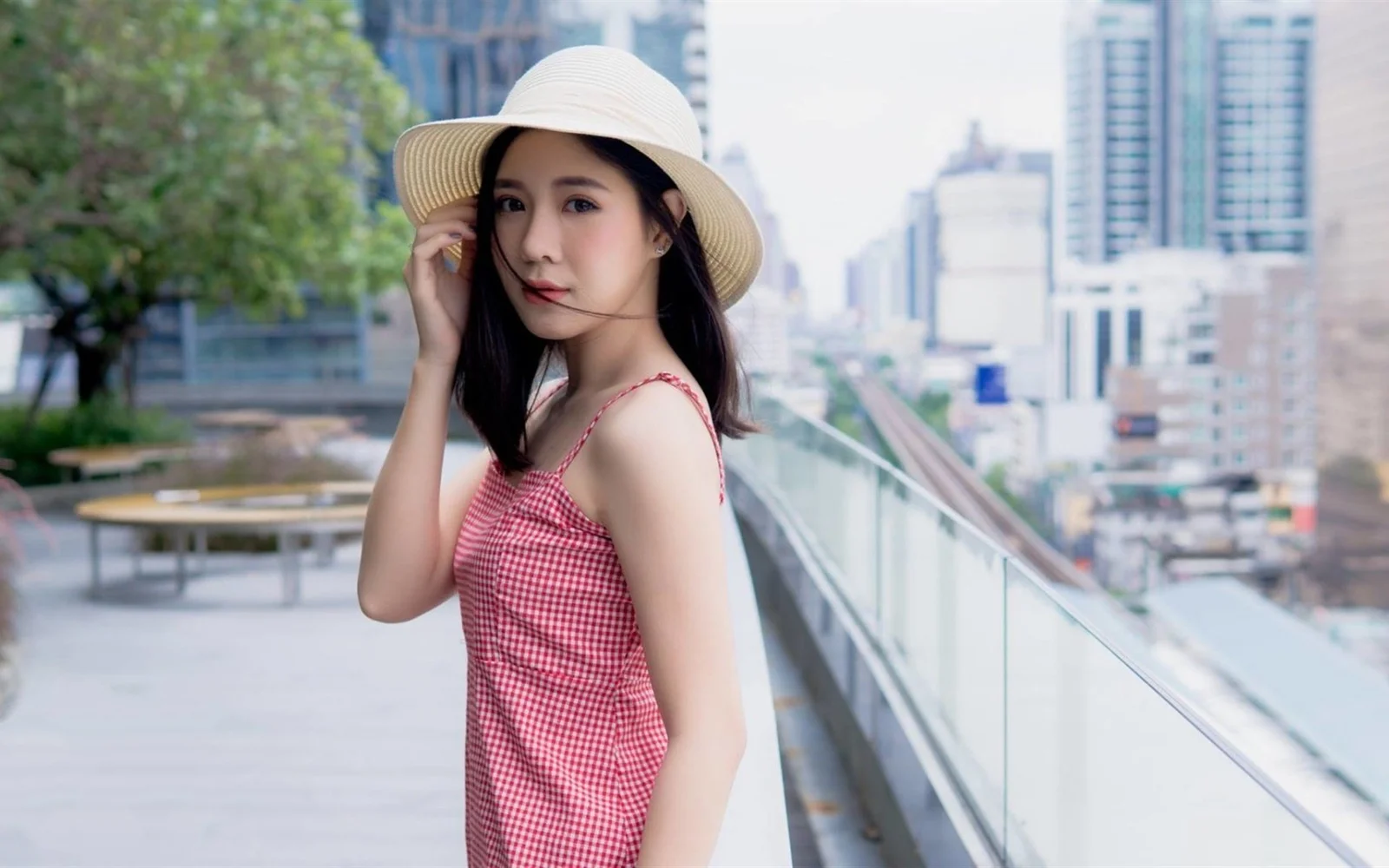 一名戴着宽檐帽的女子站在城市露台的玻璃栏杆旁。