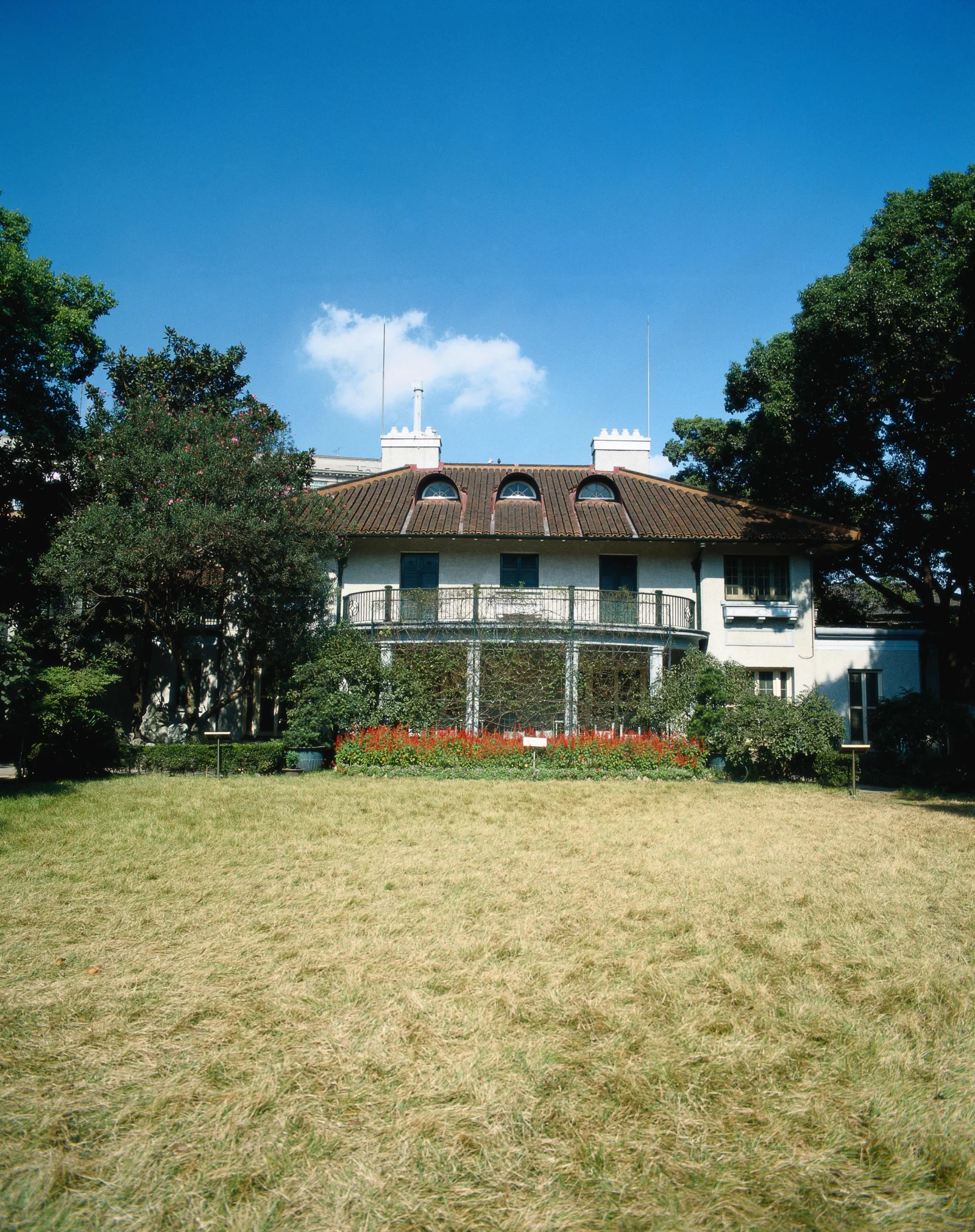 一座白色建筑坐落在树木、花坛和草坪之间，屋顶上方是晴朗的蓝天。