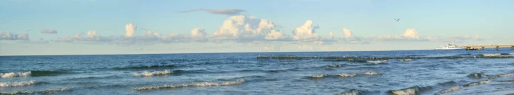 海浪轻拍海岸，远处延伸着平静的海面与明亮云层。