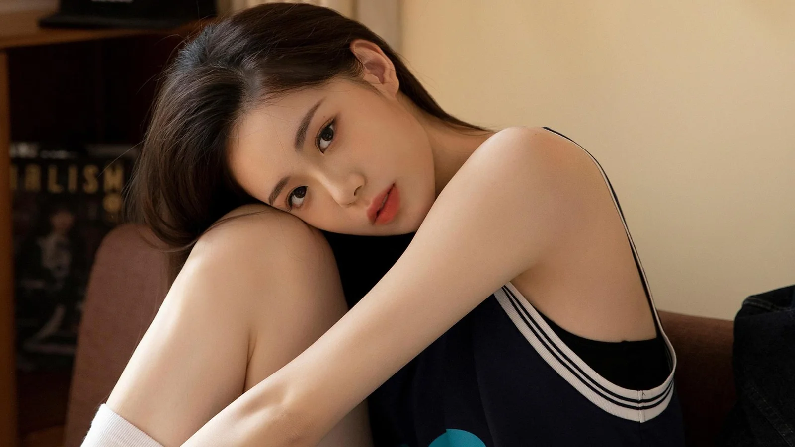 一名身穿黑色无袖服装的女性抱膝坐在沙发上，注视着镜头。
