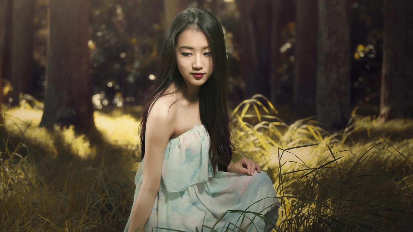 一名身穿浅绿色连衣裙的女子坐在阳光斑驳的森林草地中。