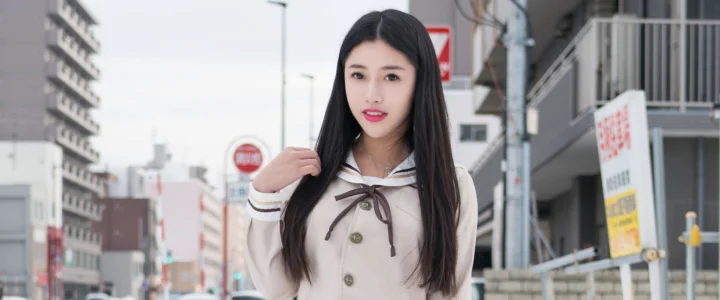 一名黑色长发女子站在城市街道上，身后可见建筑和街道设施。