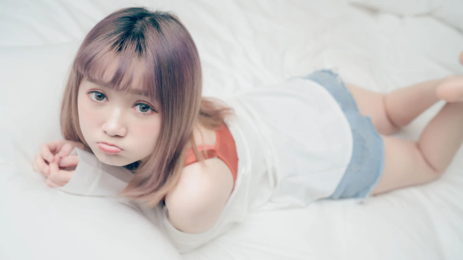 단발머리 여성이 흰색 침대에 엎드려 카메라를 바라보고 있다.