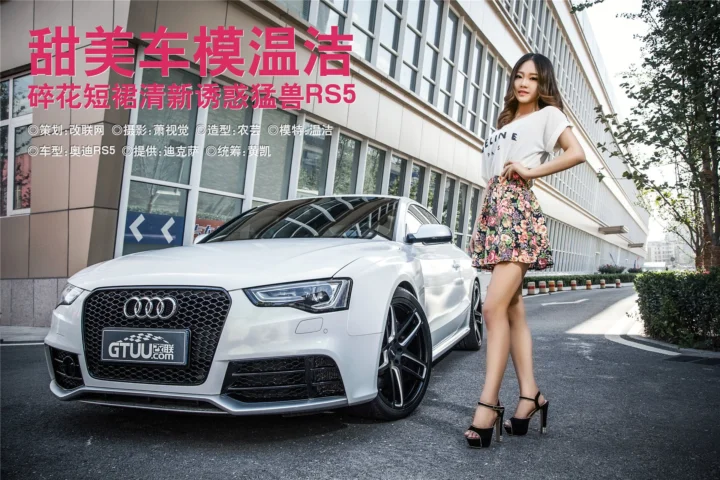一辆白色轿车停在建筑外，一名身穿白色上衣和花卉短裙的成年女性站在车旁。