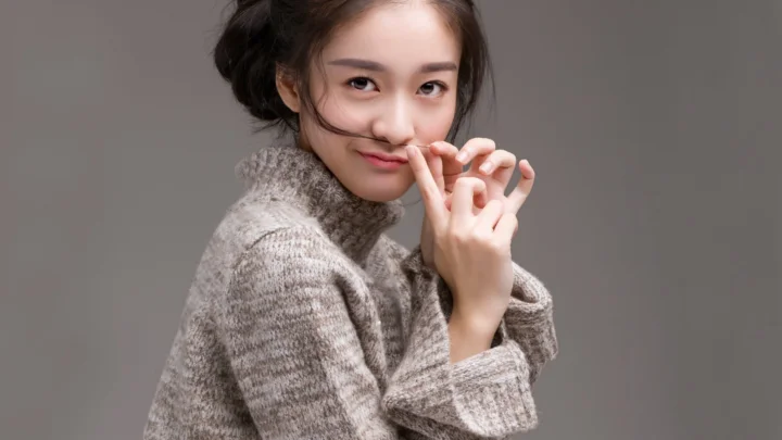 一名成年女性穿着灰色针织衫，在灰色背景前摆出自然姿态。