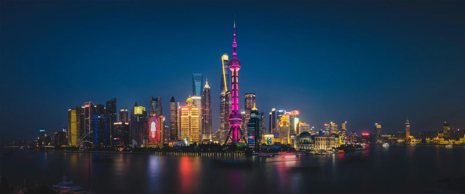 夜幕下的城市天際線沿著水面展開，彩色燈光倒映在平靜的水中。