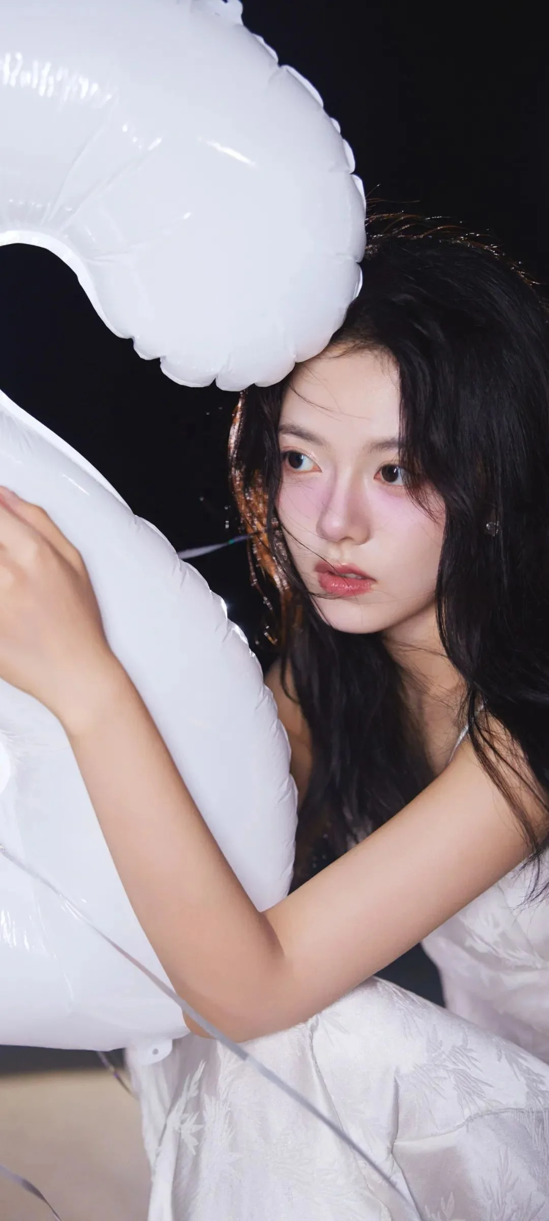 長い黒髪の女性が暗い背景の前で大きな白い浮き輪を抱えている。