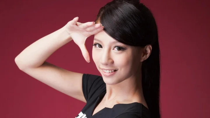 一名黑发女性在红色背景前微笑并抬手摆出姿势。