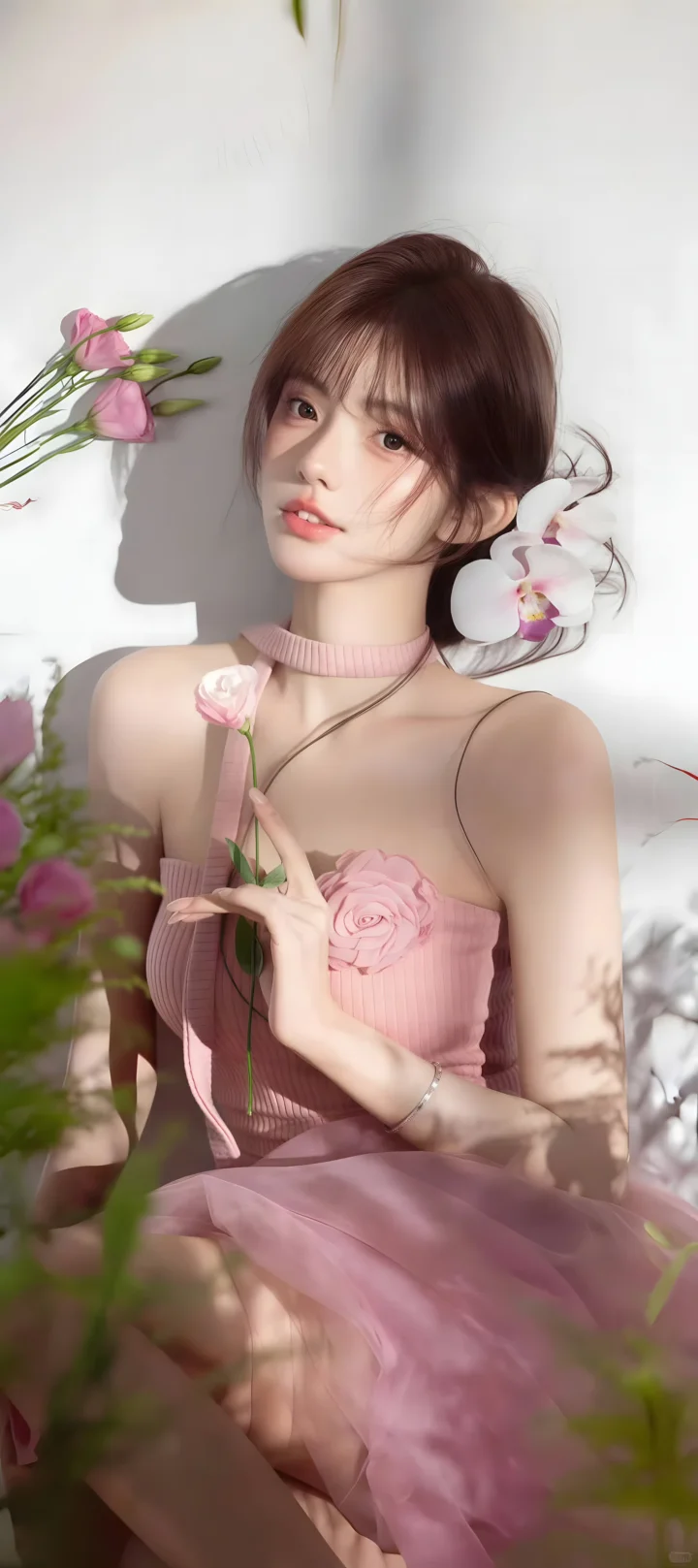 ピンクのドレスを着た成人女性が花を手にし、ピンクの花々と柔らかな影に囲まれています。