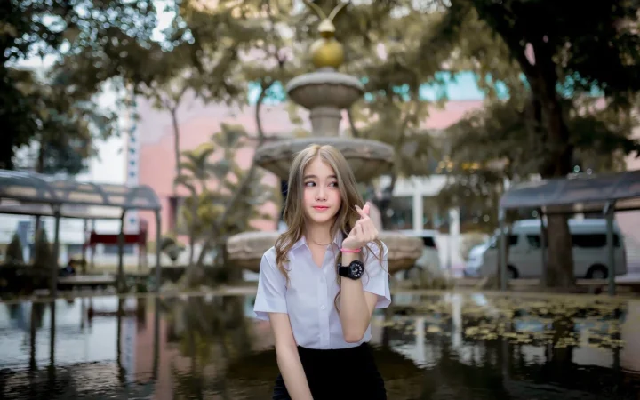 一名成年女子站在户外庭院的喷泉和池塘旁。