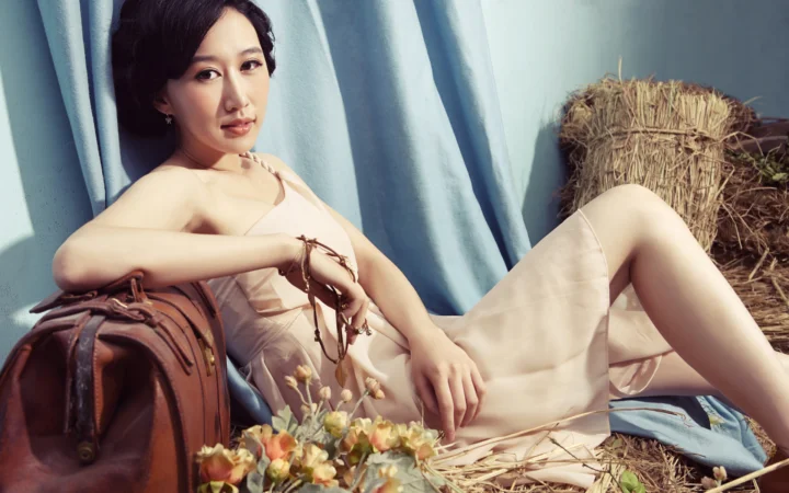一名成年女性身穿浅色连衣裙坐在帘幕、行李箱和干草垛旁。