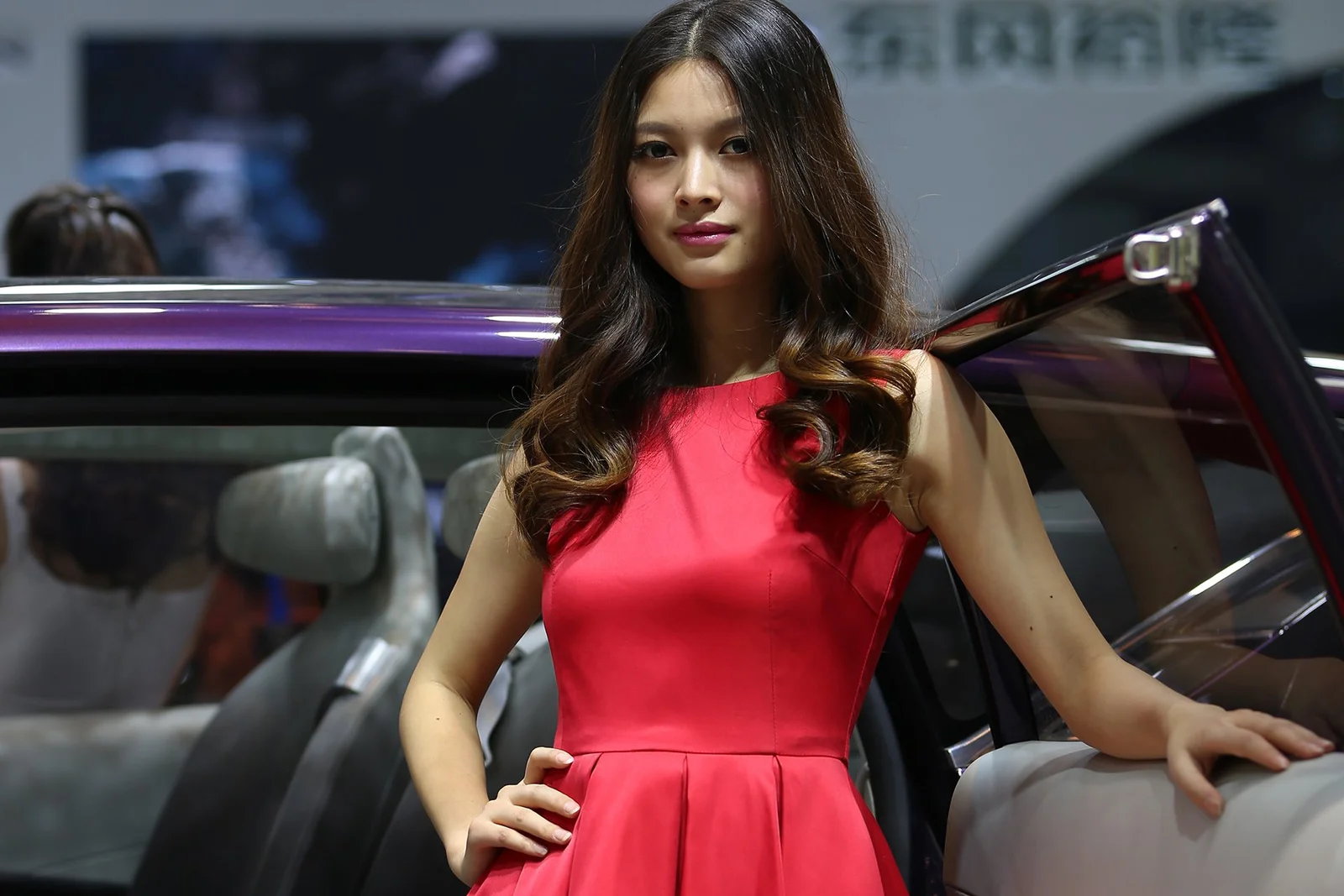 赤いドレスを着た女性が車のそばに立っています。