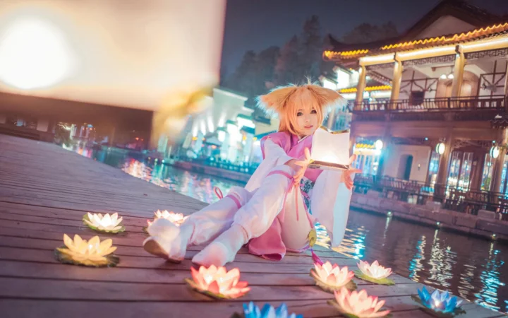 一名动漫角色扮演者坐在水畔木栈道上，周围漂浮着莲花灯，背景是灯火通明的传统建筑。