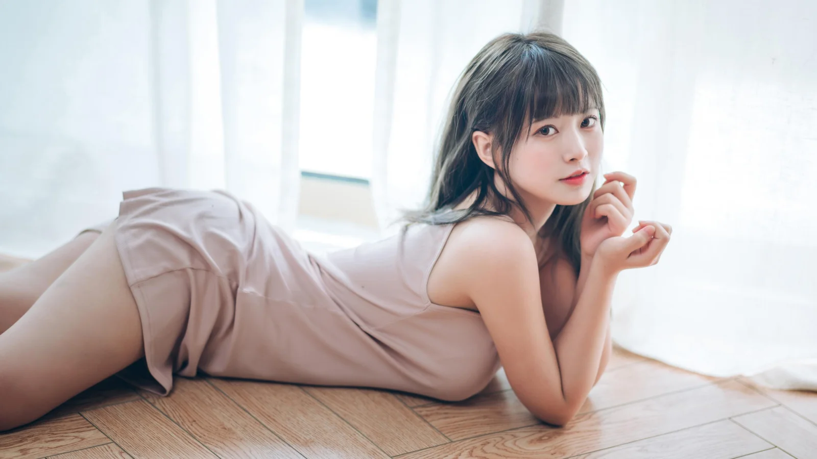 밝은 실내의 나무 바닥에 연한 색 원피스를 입은 성인 여성이 누워 있습니다.