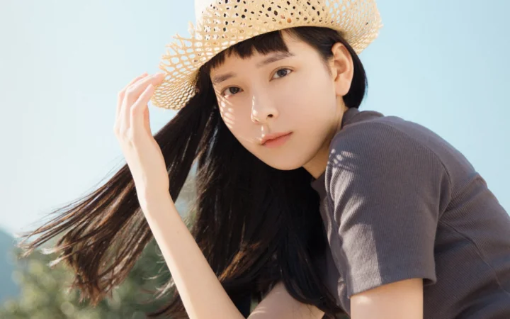 밀짚모자를 쓴 긴 머리 여성이 야외의 햇빛 속에서 카메라를 바라보고 있습니다.