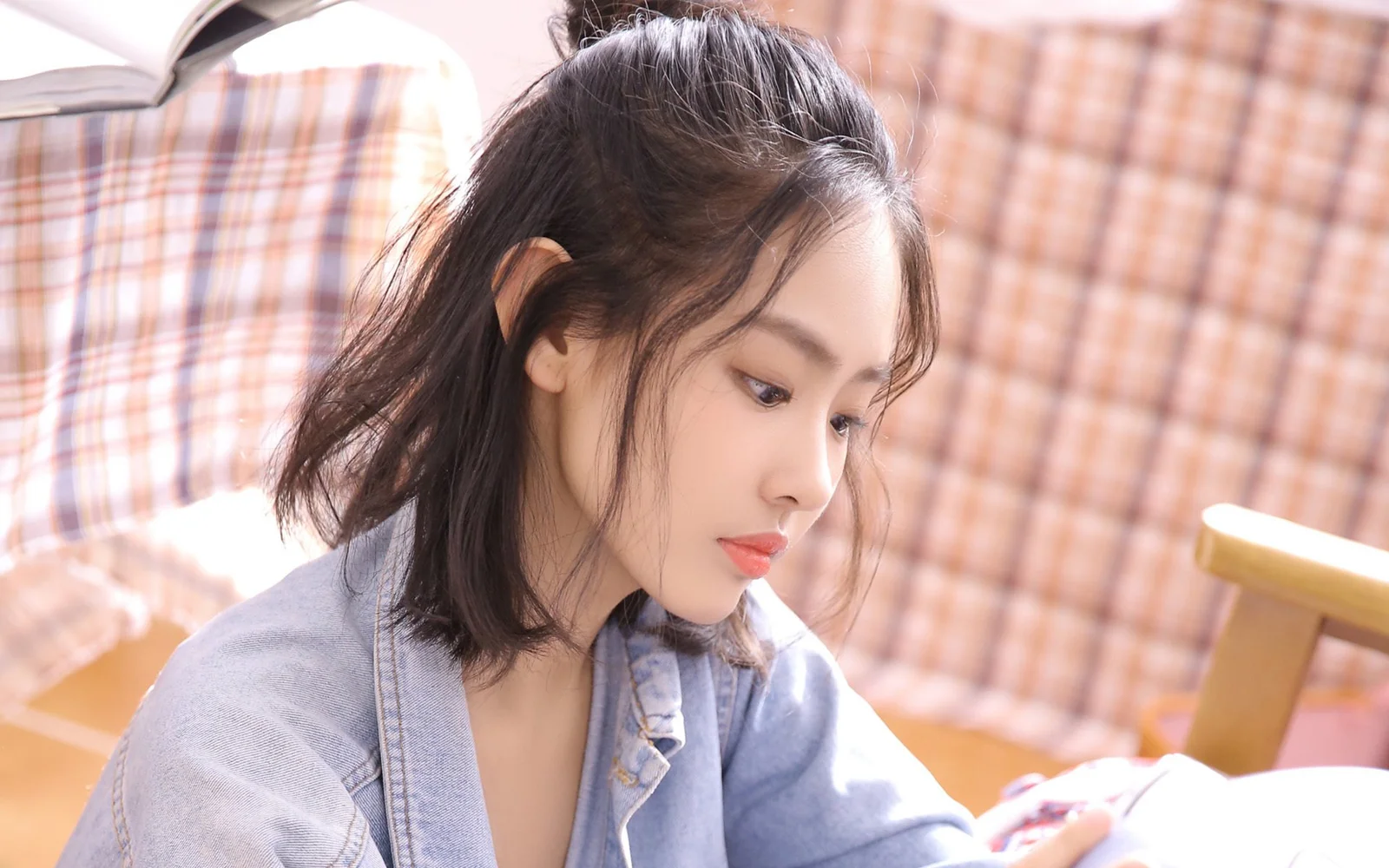 연한 데님 재킷을 입은 검은 머리 여성이 체크무늬 배경 앞에서 아래를 바라보고 있습니다.