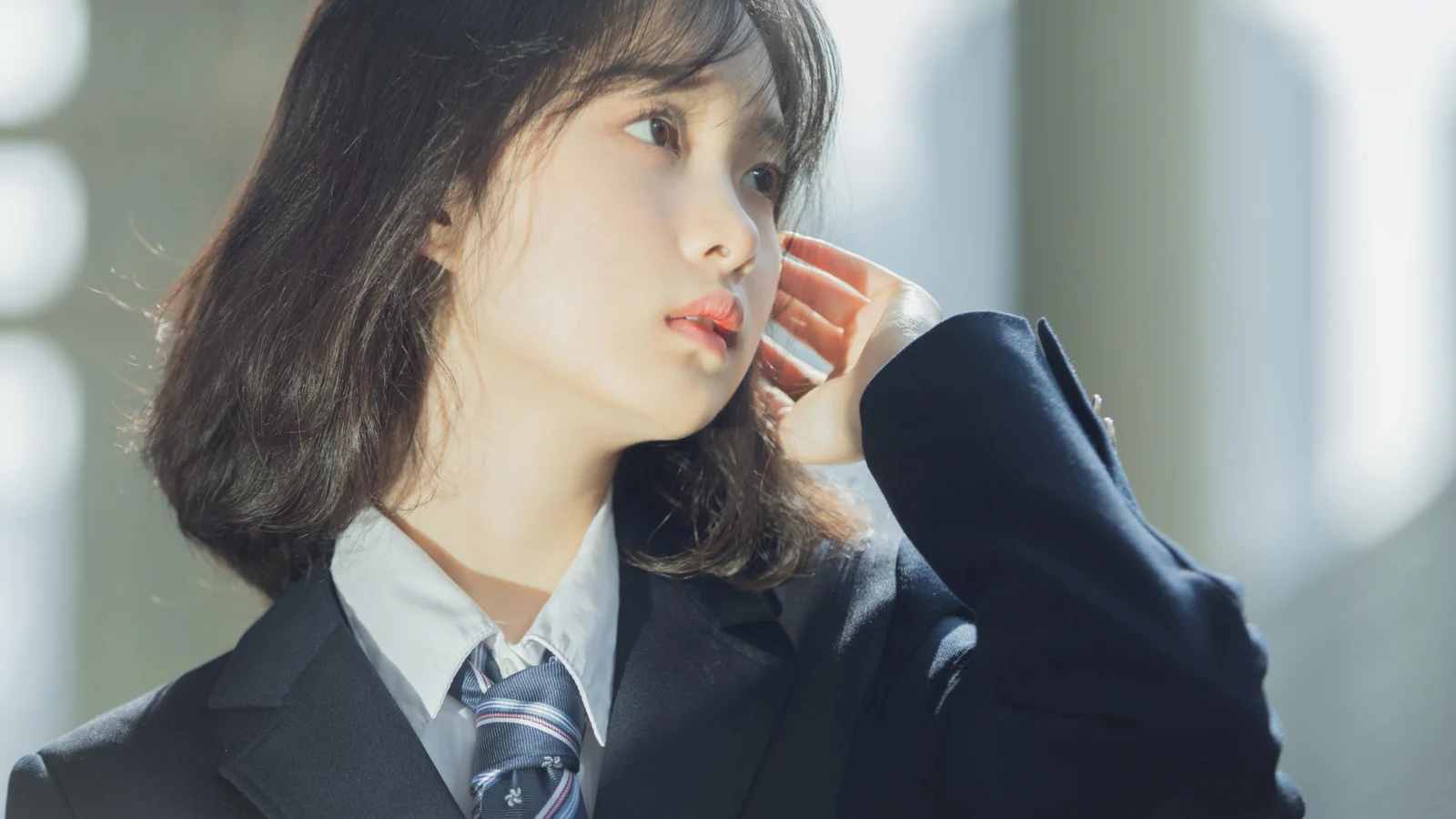 一名身穿深色西装的女性站在明亮窗边，侧头望向一旁。